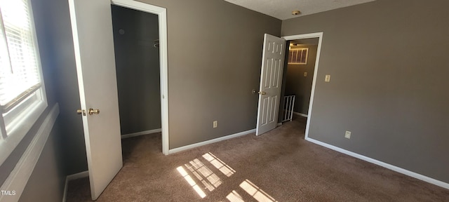 unfurnished bedroom featuring a spacious closet, dark carpet, and a closet