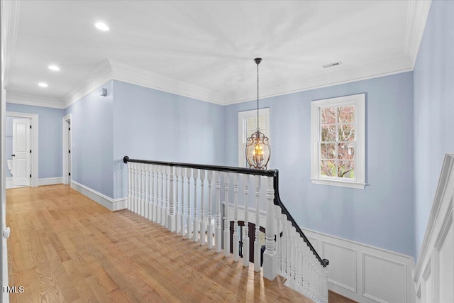 corridor featuring a chandelier, ornamental molding, wainscoting, and an upstairs landing