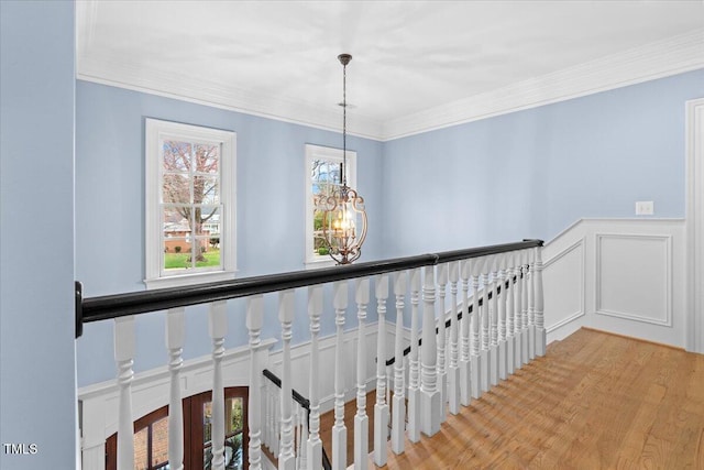 hallway featuring wainscoting, ornamental molding, wood finished floors, an upstairs landing, and a notable chandelier