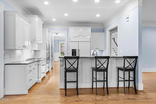 kitchen with dark countertops, light wood-type flooring, a breakfast bar, and built in appliances