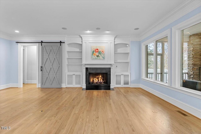 unfurnished living room with a barn door, a fireplace with flush hearth, visible vents, ornamental molding, and light wood finished floors