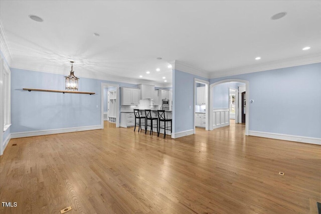 unfurnished living room featuring arched walkways, light wood finished floors, ornamental molding, and a notable chandelier