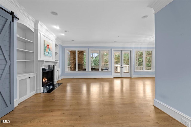 unfurnished living room featuring a barn door, a high end fireplace, baseboards, light wood-style floors, and crown molding