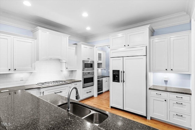 kitchen featuring ornamental molding, white cabinetry, a sink, and built in appliances