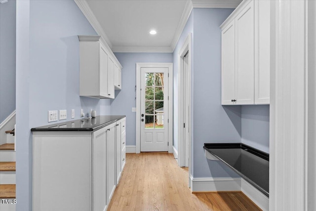 kitchen featuring baseboards, dark countertops, light wood-style flooring, crown molding, and white cabinetry