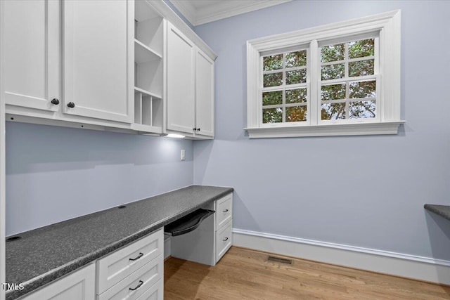 unfurnished office featuring visible vents, baseboards, ornamental molding, light wood-type flooring, and built in study area