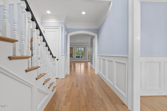 interior space with ornamental molding, arched walkways, a decorative wall, and light wood finished floors