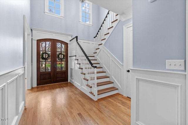 entrance foyer featuring french doors, a wealth of natural light, a decorative wall, light wood-style flooring, and stairs