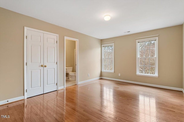 unfurnished bedroom with ensuite bath, light hardwood / wood-style floors, and a closet