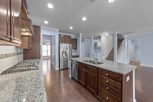 kitchen featuring sink, appliances with stainless steel finishes, light stone countertops, a kitchen island with sink, and backsplash