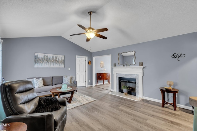 living area with lofted ceiling, a premium fireplace, light wood-style floors, ceiling fan, and baseboards