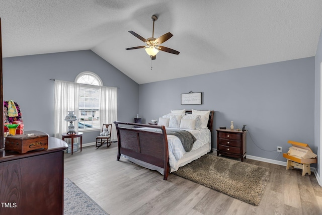 bedroom featuring baseboards, lofted ceiling, ceiling fan, a textured ceiling, and light wood-type flooring