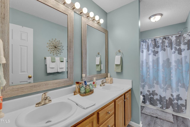 full bathroom with a sink, a textured ceiling, toilet, and double vanity