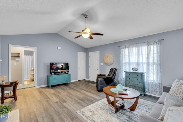 living area featuring a textured ceiling, a ceiling fan, baseboards, vaulted ceiling, and light wood-style floors