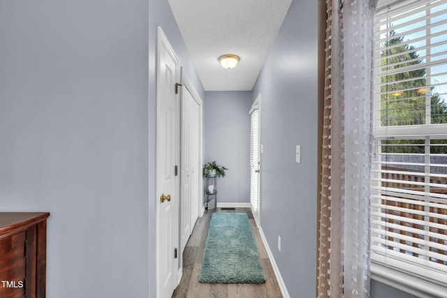 corridor featuring a textured ceiling, baseboards, and wood finished floors