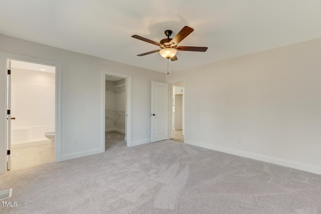 unfurnished bedroom with connected bathroom, a walk in closet, light colored carpet, ceiling fan, and a closet