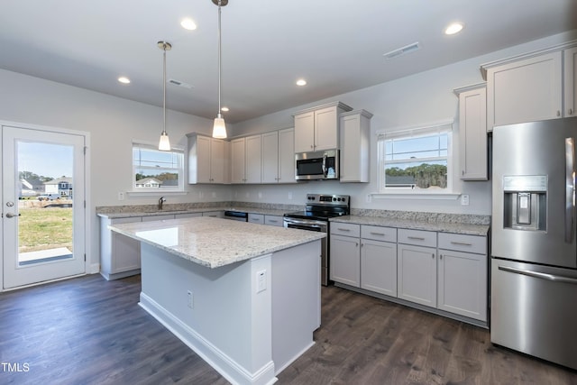 kitchen with hanging light fixtures, stainless steel appliances, a center island, light stone countertops, and a healthy amount of sunlight