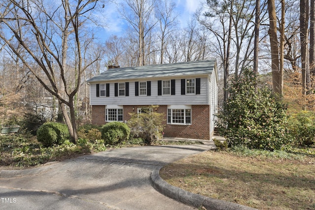 colonial-style house with aphalt driveway, brick siding, and a chimney