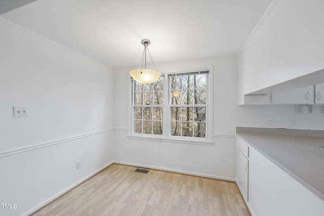 unfurnished dining area with light wood-style floors, baseboards, visible vents, and ornamental molding