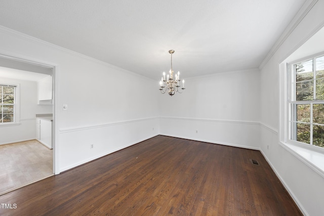 empty room with a wealth of natural light, visible vents, an inviting chandelier, and wood finished floors