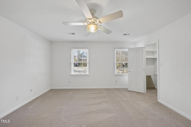 unfurnished bedroom featuring a spacious closet, visible vents, a textured ceiling, and light colored carpet