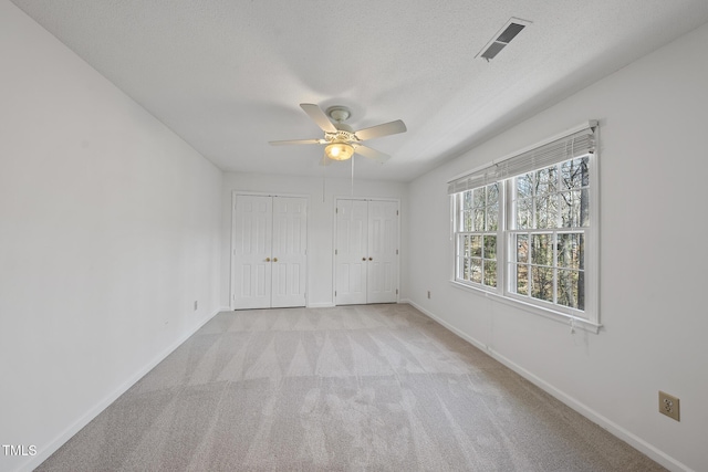 unfurnished bedroom featuring baseboards, visible vents, a textured ceiling, carpet flooring, and two closets