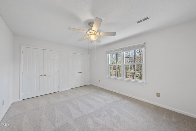 unfurnished bedroom featuring ceiling fan, carpet floors, visible vents, baseboards, and multiple closets