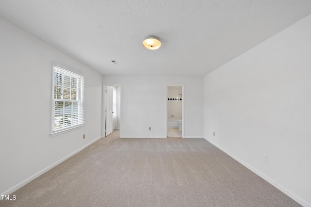 empty room featuring a textured ceiling, light colored carpet, and baseboards