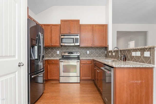 kitchen with lofted ceiling, sink, stainless steel appliances, light stone countertops, and light hardwood / wood-style flooring