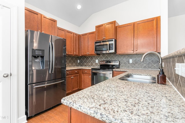 kitchen with appliances with stainless steel finishes, lofted ceiling, sink, decorative backsplash, and light hardwood / wood-style floors