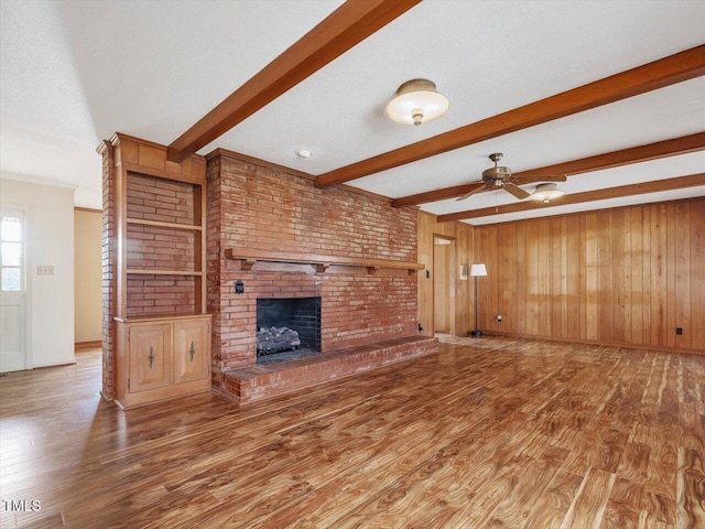 unfurnished living room featuring hardwood / wood-style floors, beam ceiling, wooden walls, and ceiling fan