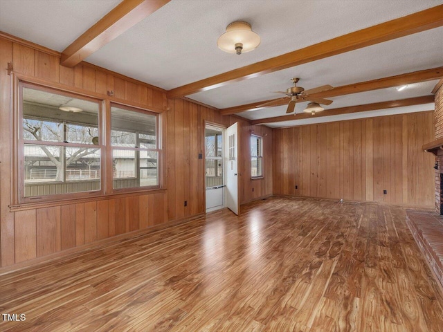 unfurnished living room featuring a textured ceiling, light wood-type flooring, wooden walls, beamed ceiling, and ceiling fan