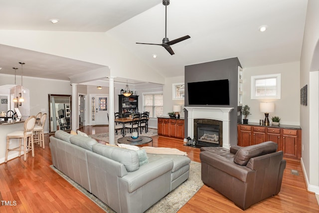 living room featuring a healthy amount of sunlight, lofted ceiling, light wood-type flooring, and ornate columns