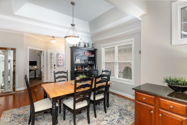 dining area with ornamental molding, a raised ceiling, and light hardwood / wood-style flooring