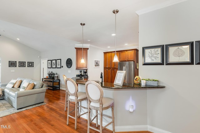 kitchen with a kitchen bar, decorative light fixtures, stainless steel refrigerator, dark hardwood / wood-style floors, and kitchen peninsula