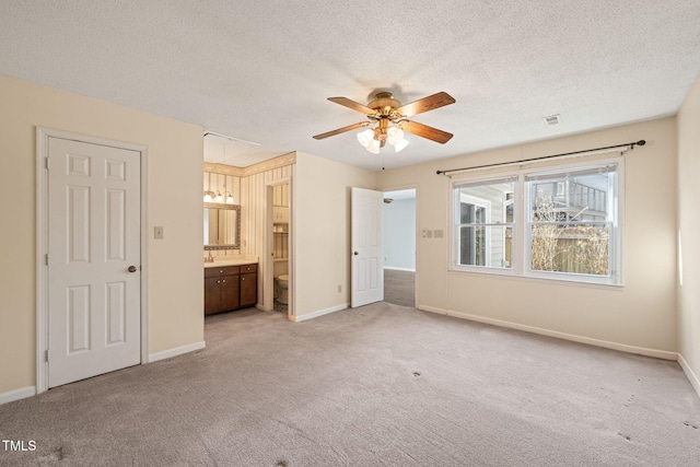 unfurnished bedroom featuring ceiling fan, ensuite bath, light colored carpet, and a textured ceiling