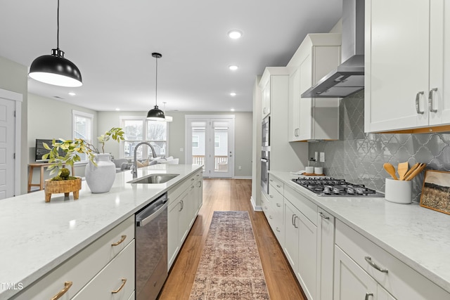 kitchen featuring pendant lighting, white cabinetry, sink, stainless steel appliances, and wall chimney range hood