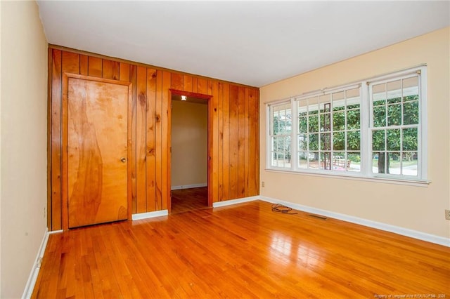 empty room featuring a healthy amount of sunlight, light wood-type flooring, and wood walls