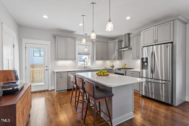 kitchen featuring appliances with stainless steel finishes, a breakfast bar area, hanging light fixtures, a center island, and wall chimney range hood