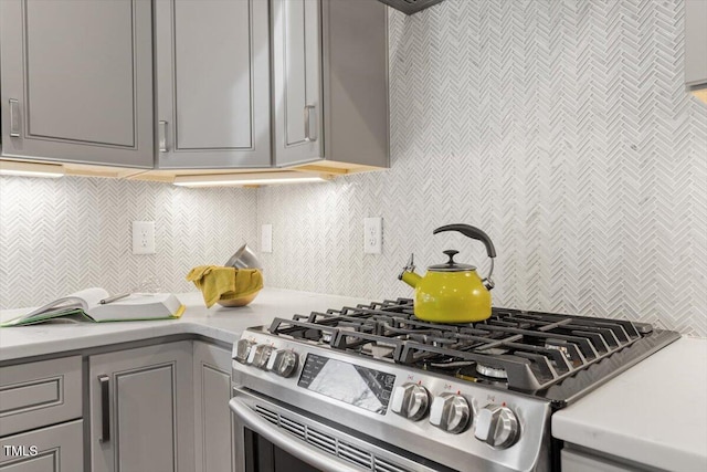 kitchen with stainless steel gas range oven, gray cabinetry, and backsplash