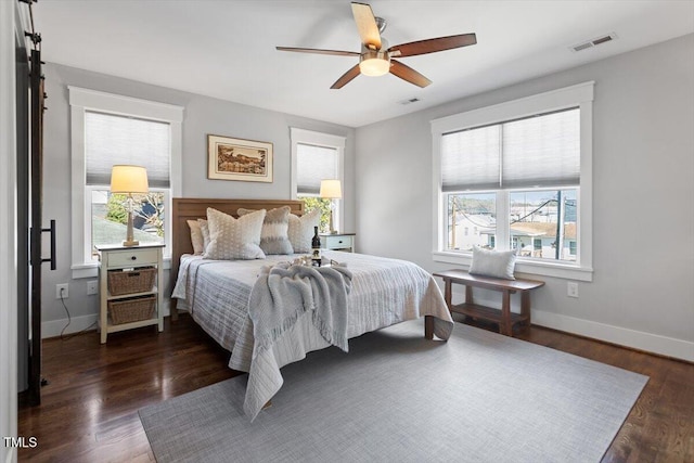 bedroom featuring a barn door, ceiling fan, dark hardwood / wood-style floors, and multiple windows