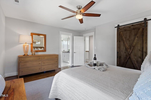 bedroom with a barn door, ceiling fan, connected bathroom, and dark hardwood / wood-style flooring