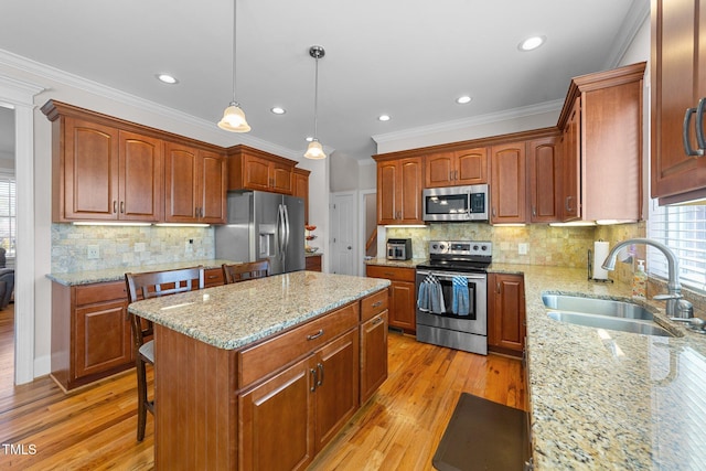 kitchen with appliances with stainless steel finishes, a sink, ornamental molding, and a kitchen island