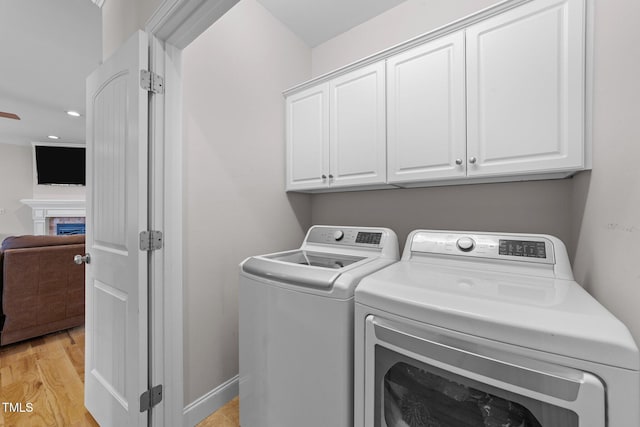 clothes washing area featuring cabinet space, washing machine and clothes dryer, light wood-type flooring, a fireplace, and recessed lighting