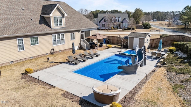 view of pool with an outbuilding, a fenced backyard, a fenced in pool, a shed, and a patio area