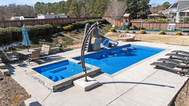 view of pool featuring a water slide, a playground, a fenced backyard, a pool with connected hot tub, and a patio area