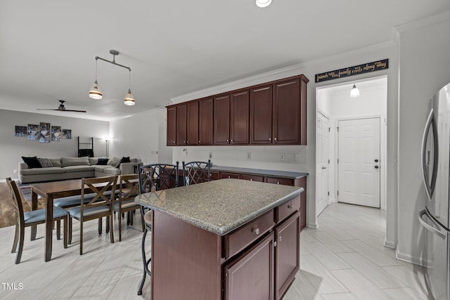 kitchen with pendant lighting, crown molding, stainless steel fridge, a center island, and light stone counters