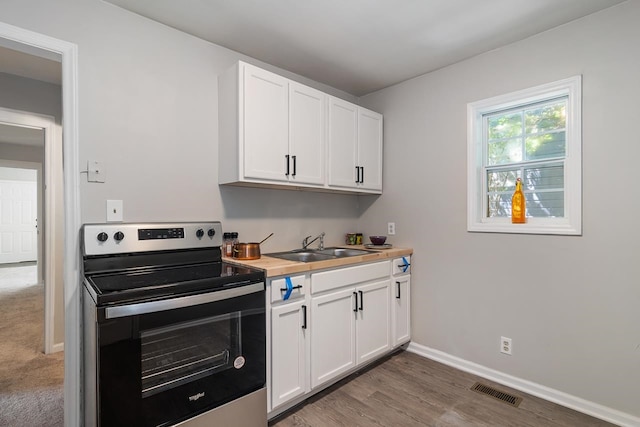 kitchen with sink, dark wood-type flooring, stainless steel range with electric cooktop, and white cabinets