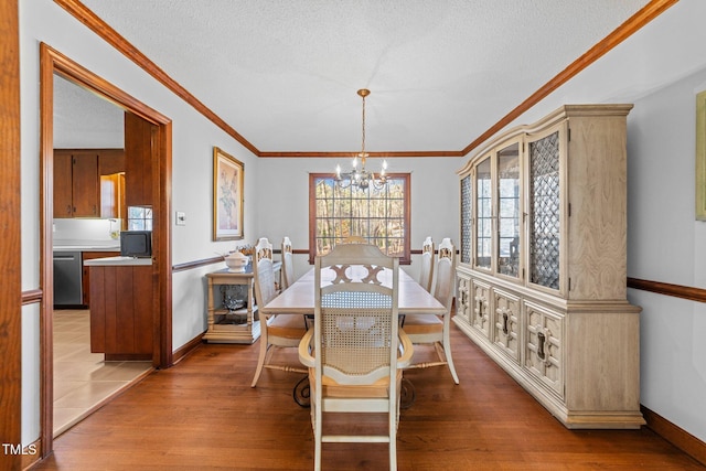 dining space with wood-type flooring, ornamental molding, a textured ceiling, and an inviting chandelier