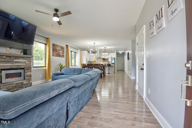 living room with ceiling fan with notable chandelier, a fireplace, and light wood-type flooring